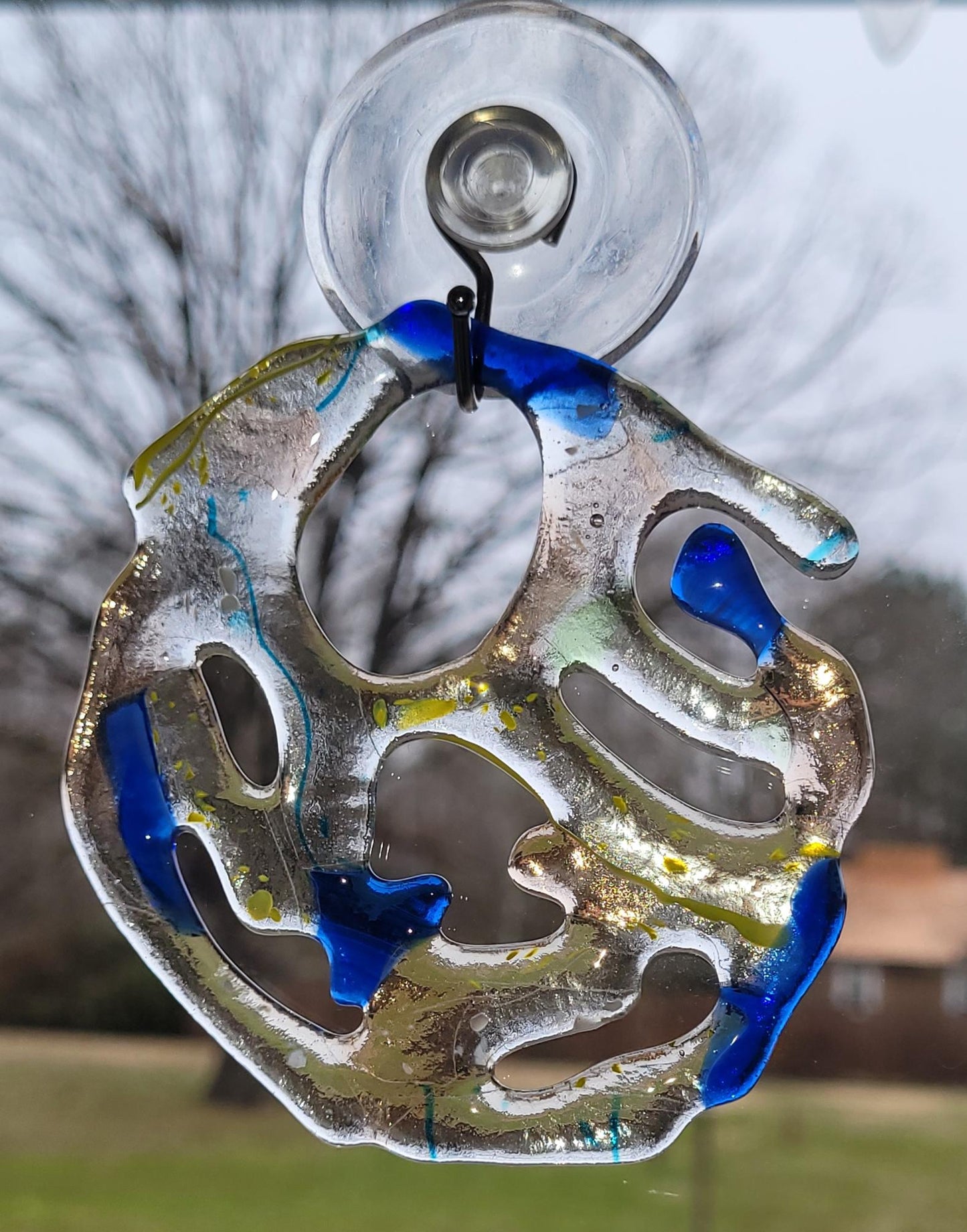 Decorative glass sun catcher with blue and silver design on a blurred outdoor background