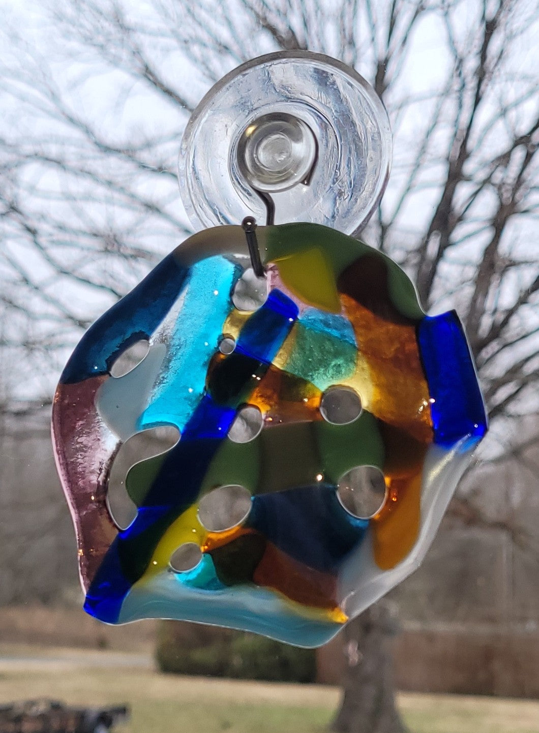 Colorful glass suncatcher hanging outdoors with trees in the background