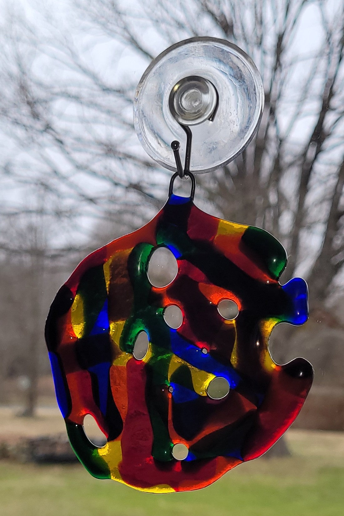 Colorful glass suncatcher with a suction cup against a blurred natural background