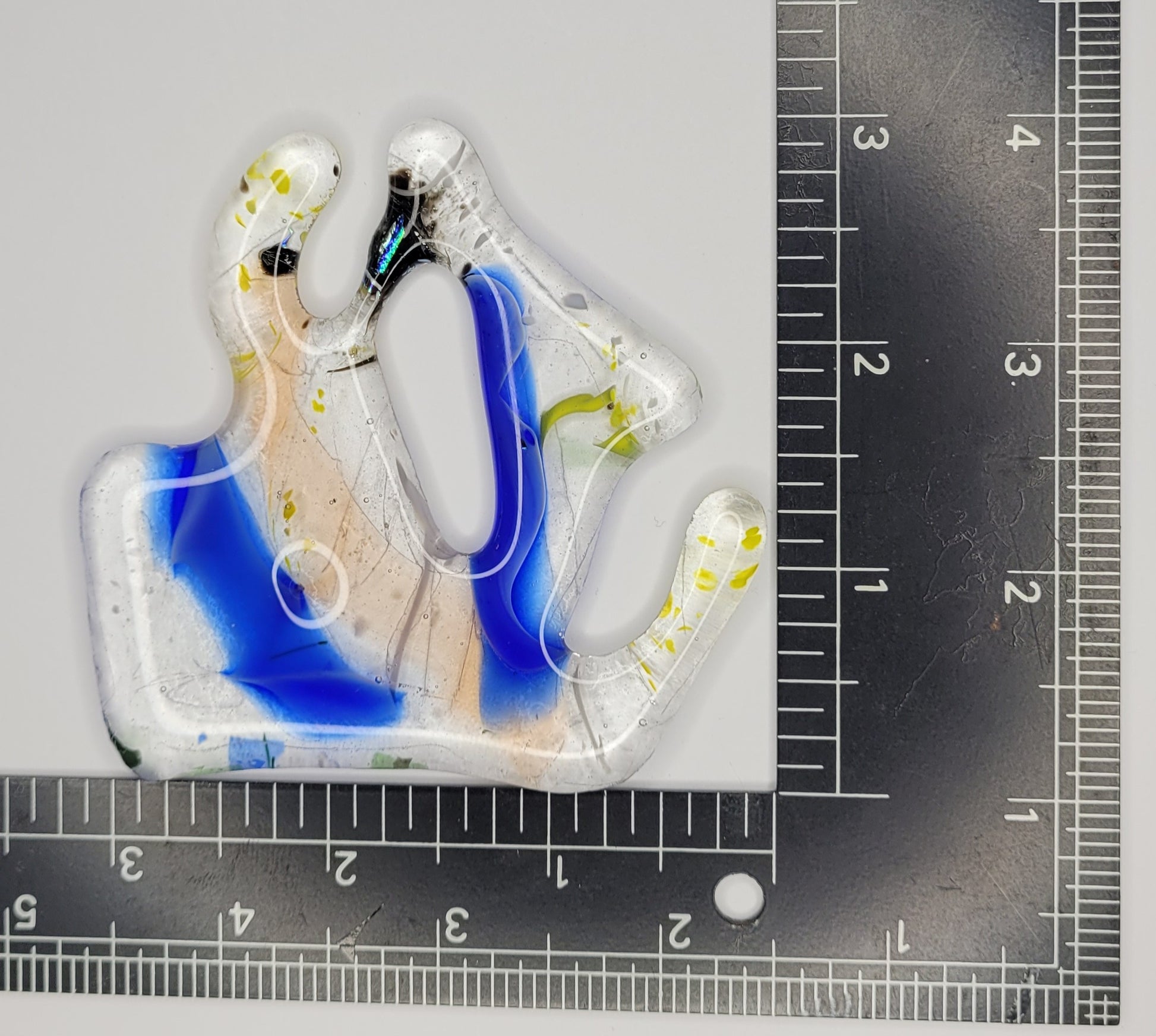 Glass suncatcher with blue and clear design on a white background with ruler for scale
