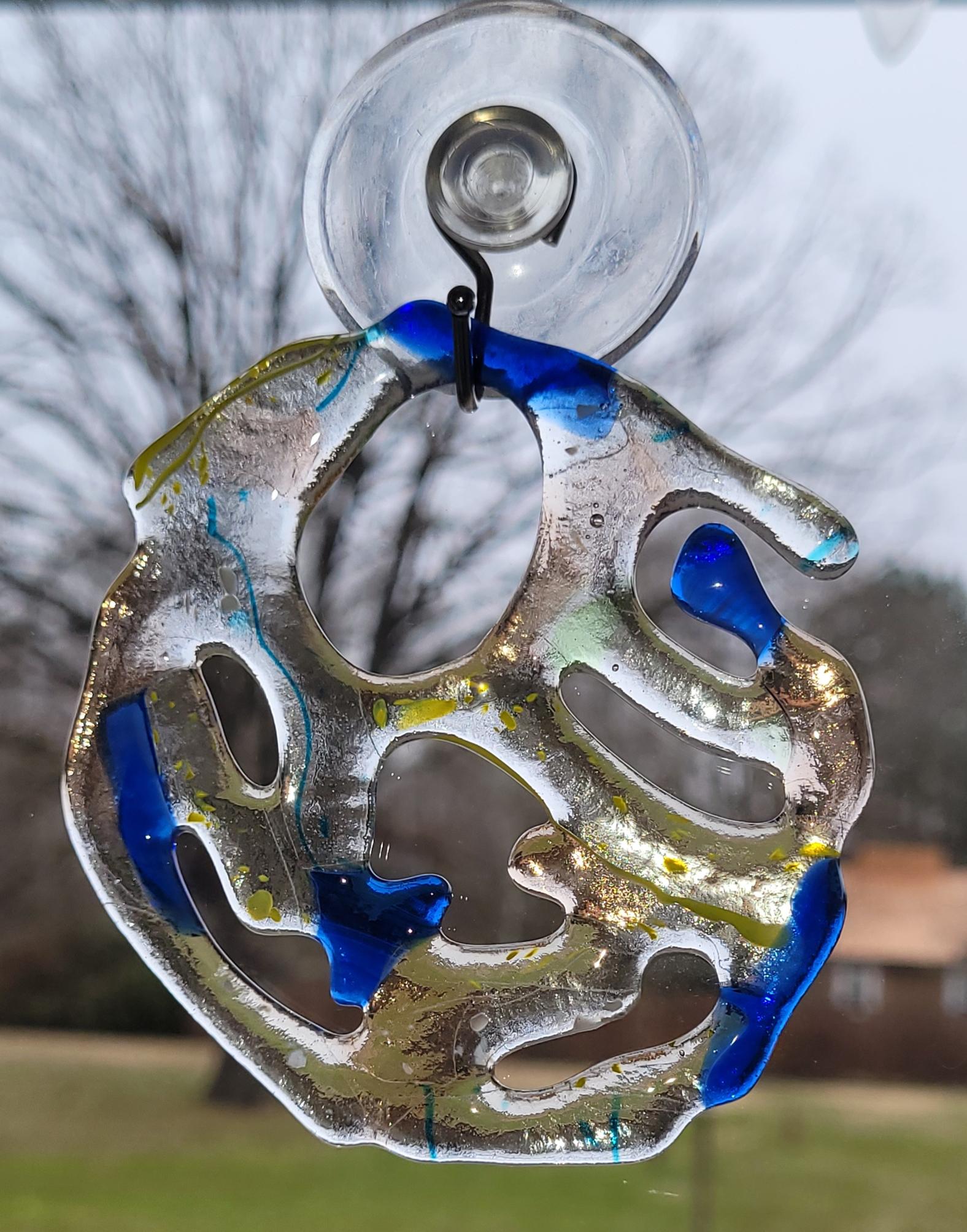 Decorative glass sun catcher with blue and silver design on a blurred outdoor background