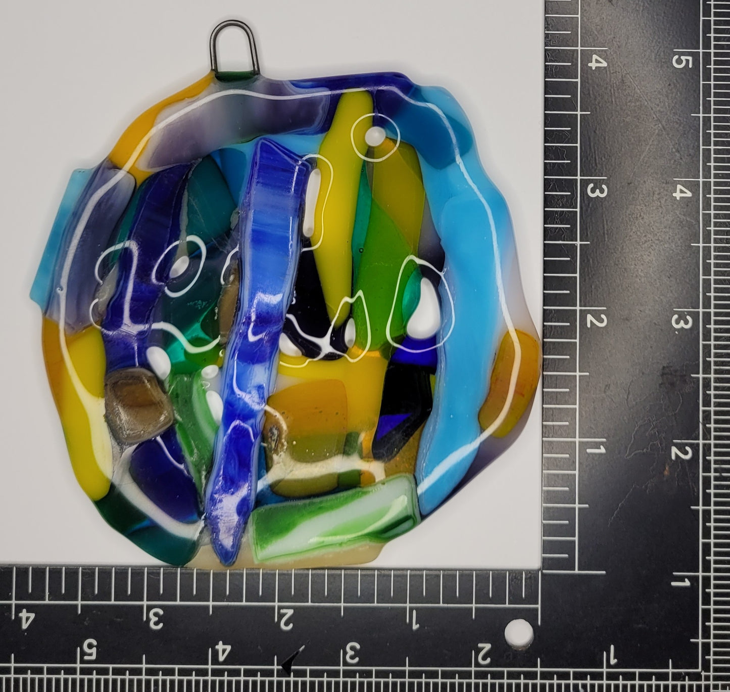 Colorful glass pendant with a ruler for scale on a white background