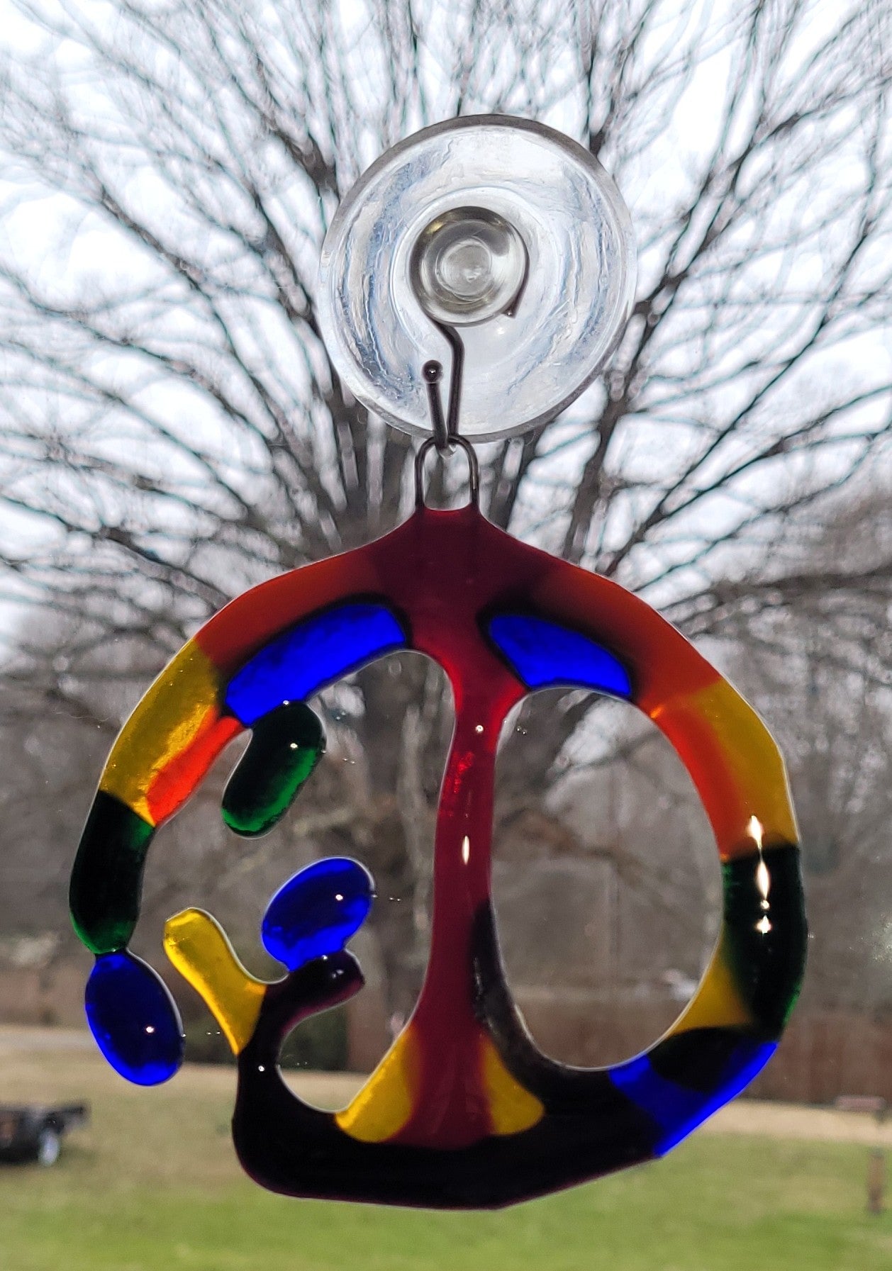 Colorful glass sun catcher with a tree design hanging outdoors.