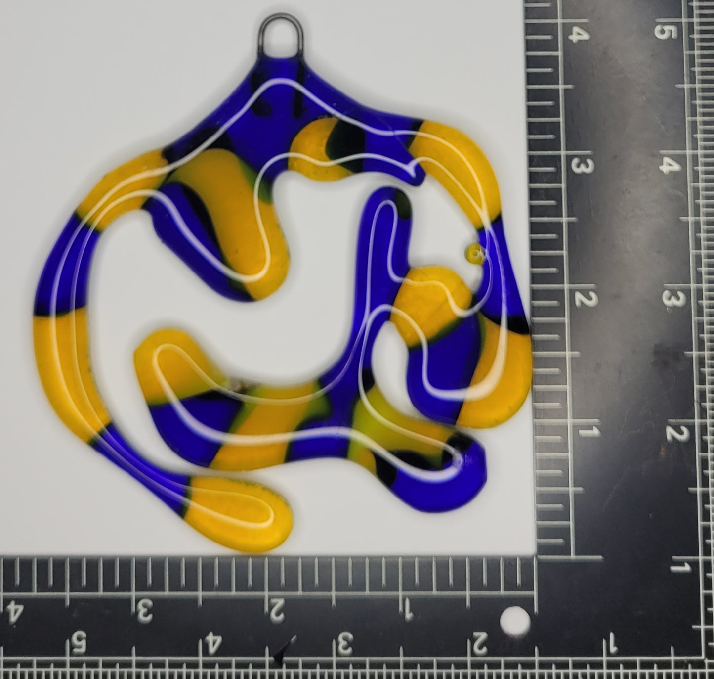 Colorful glass pendant with a pattern next to a ruler for scale