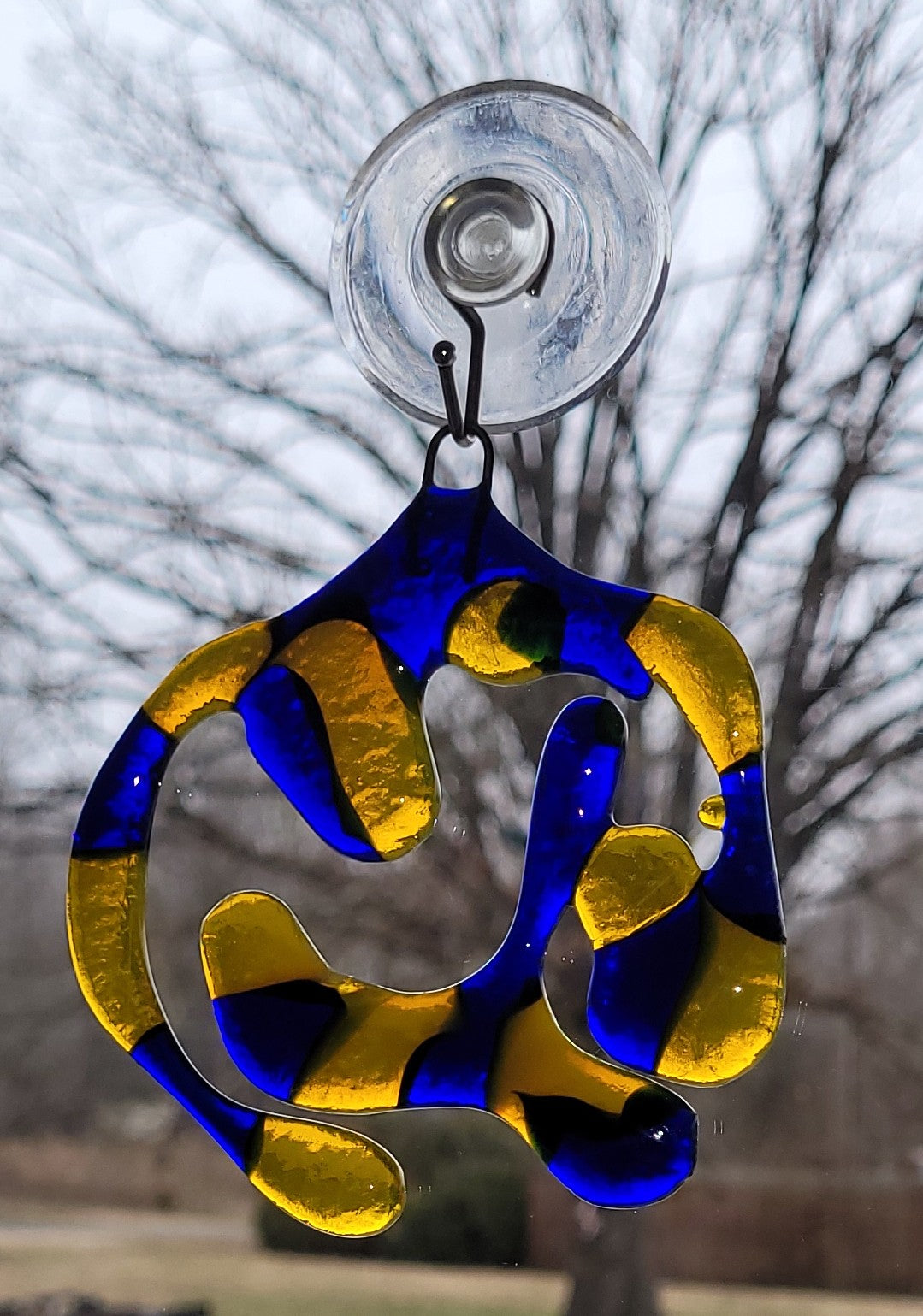 Decorative blue and yellow hanging ornament with a suction cup against a blurred natural background