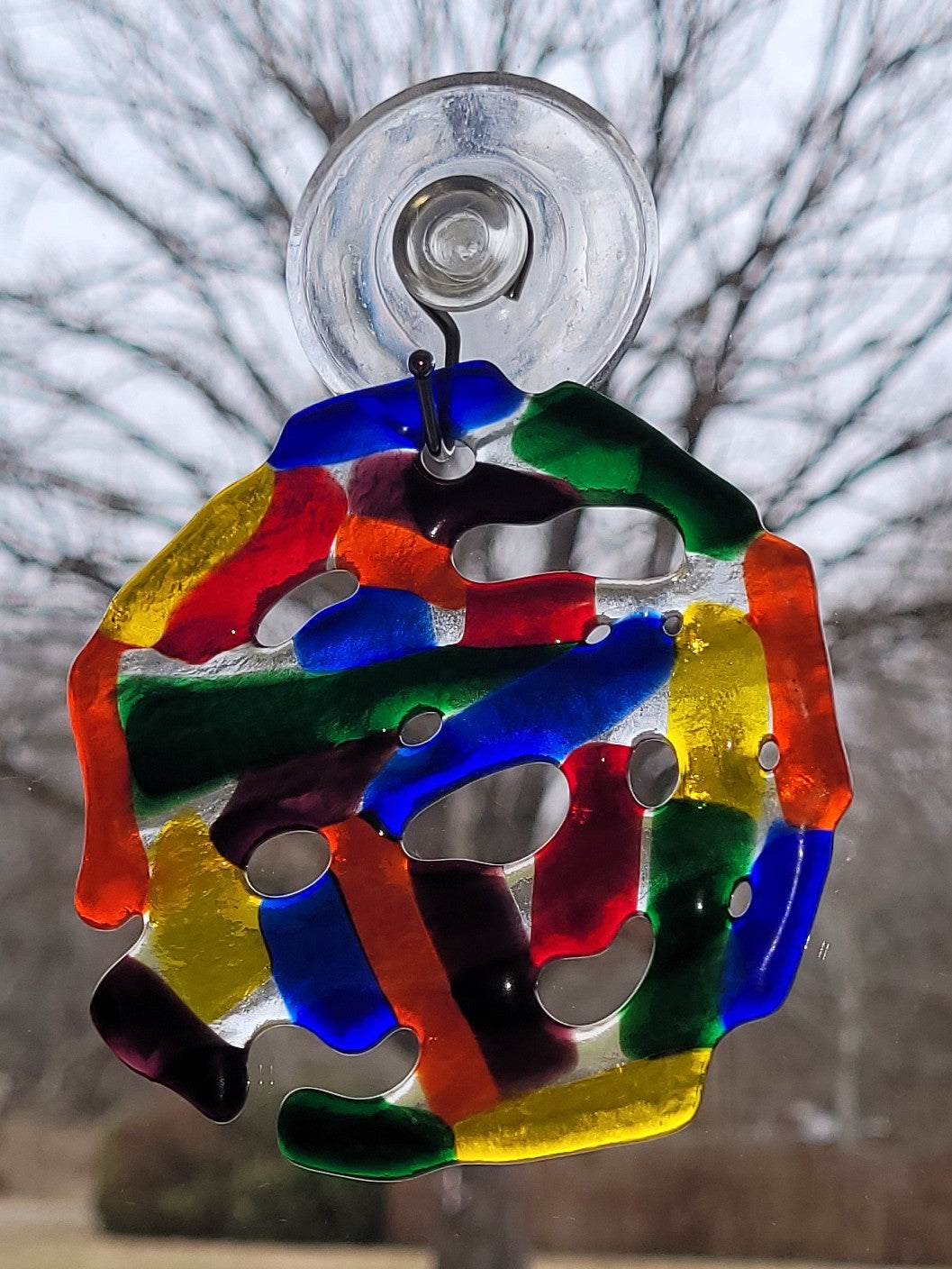 Colorful glass sun catcher with suction cup against a blurred outdoor background