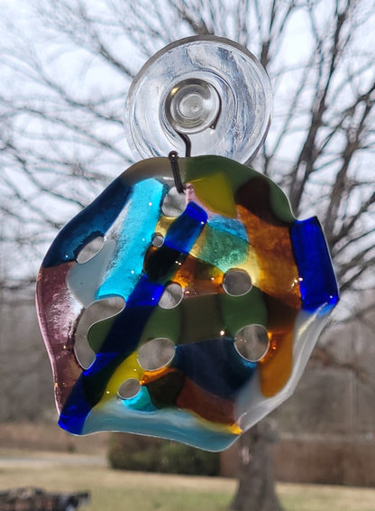 Colorful glass suncatcher hanging outdoors with trees in the background