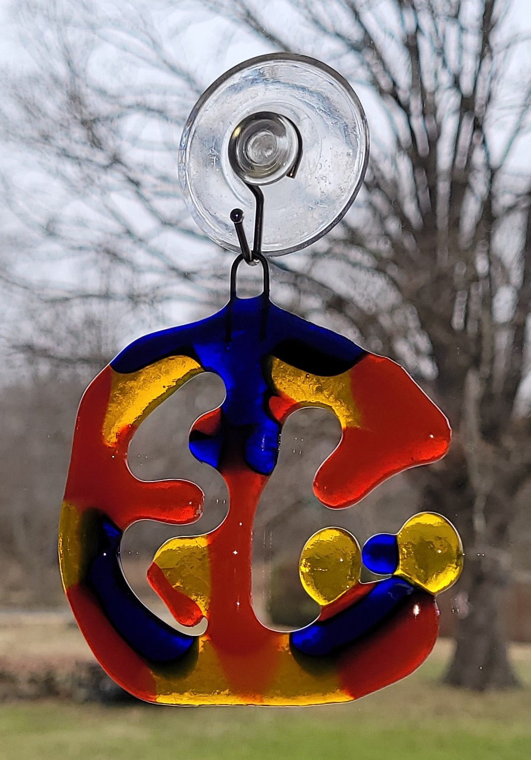 Colorful glass hanging ornament with suction cup against a blurred natural background