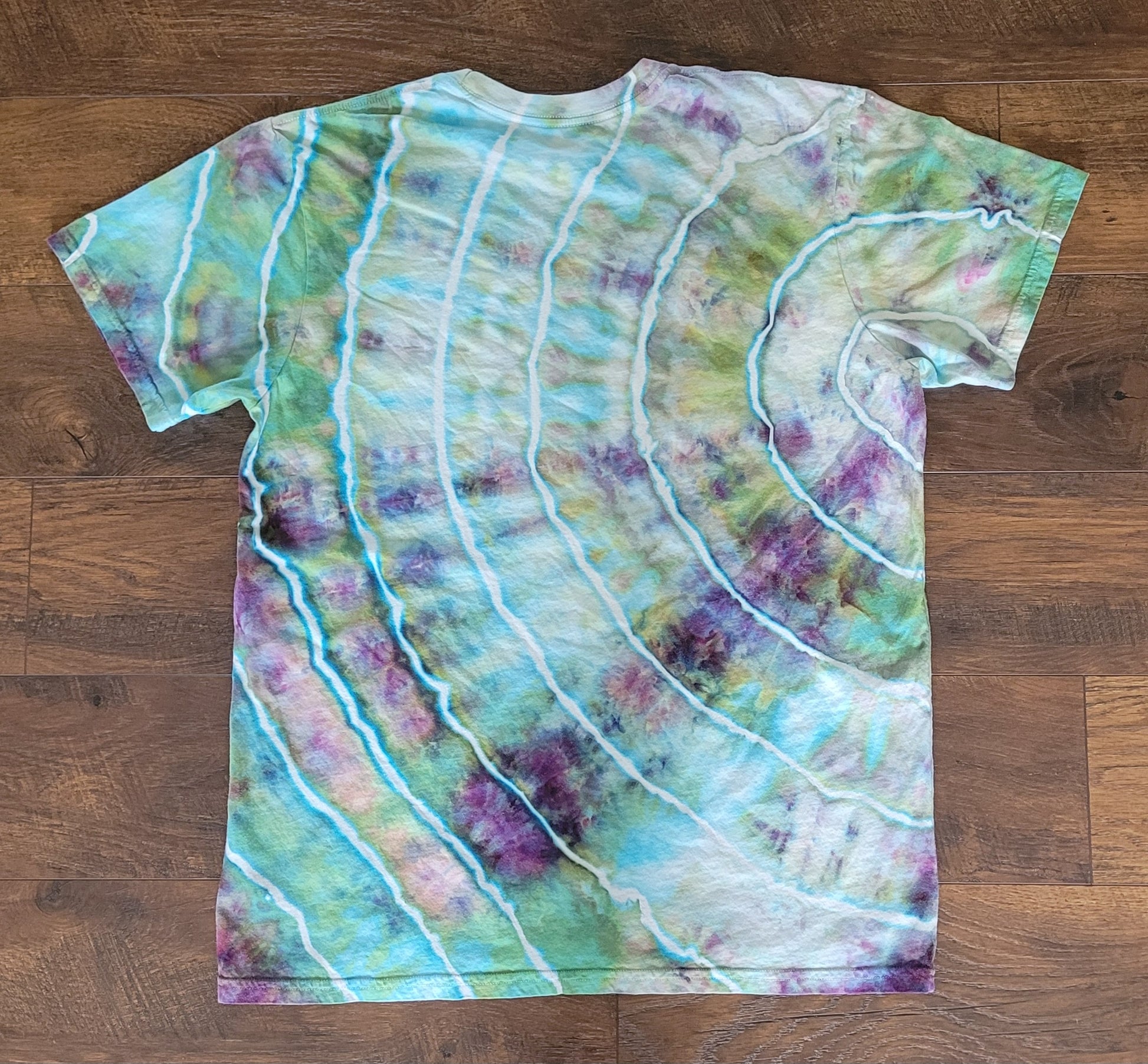 Tie-dye t-shirt with green, purple, and white patterns on a wooden surface