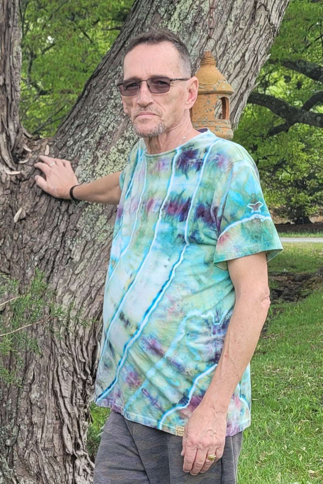 Man wearing a tie-dye shirt leaning against a tree