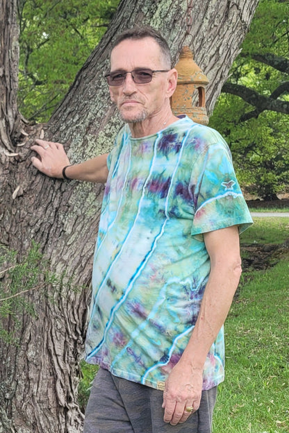 Man wearing a tie-dye shirt leaning against a tree