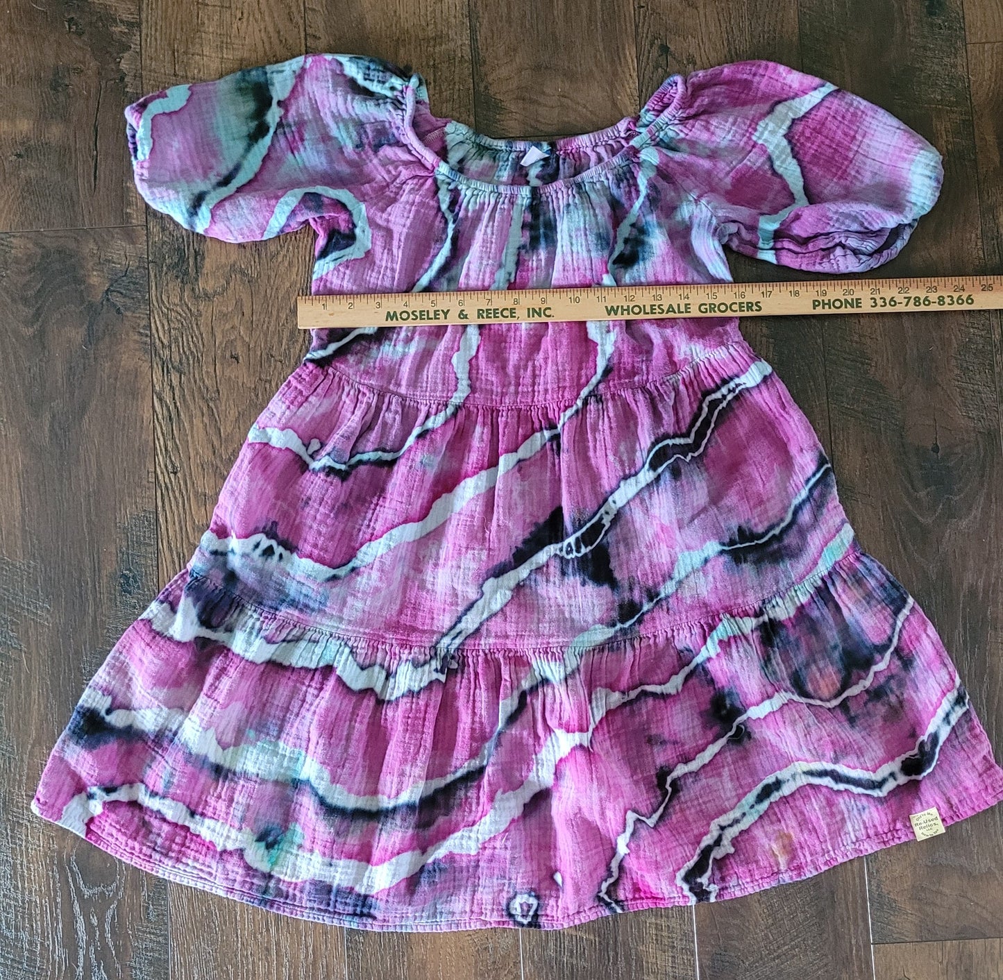 Pink patterned dress on a wooden surface with a ruler for scale.