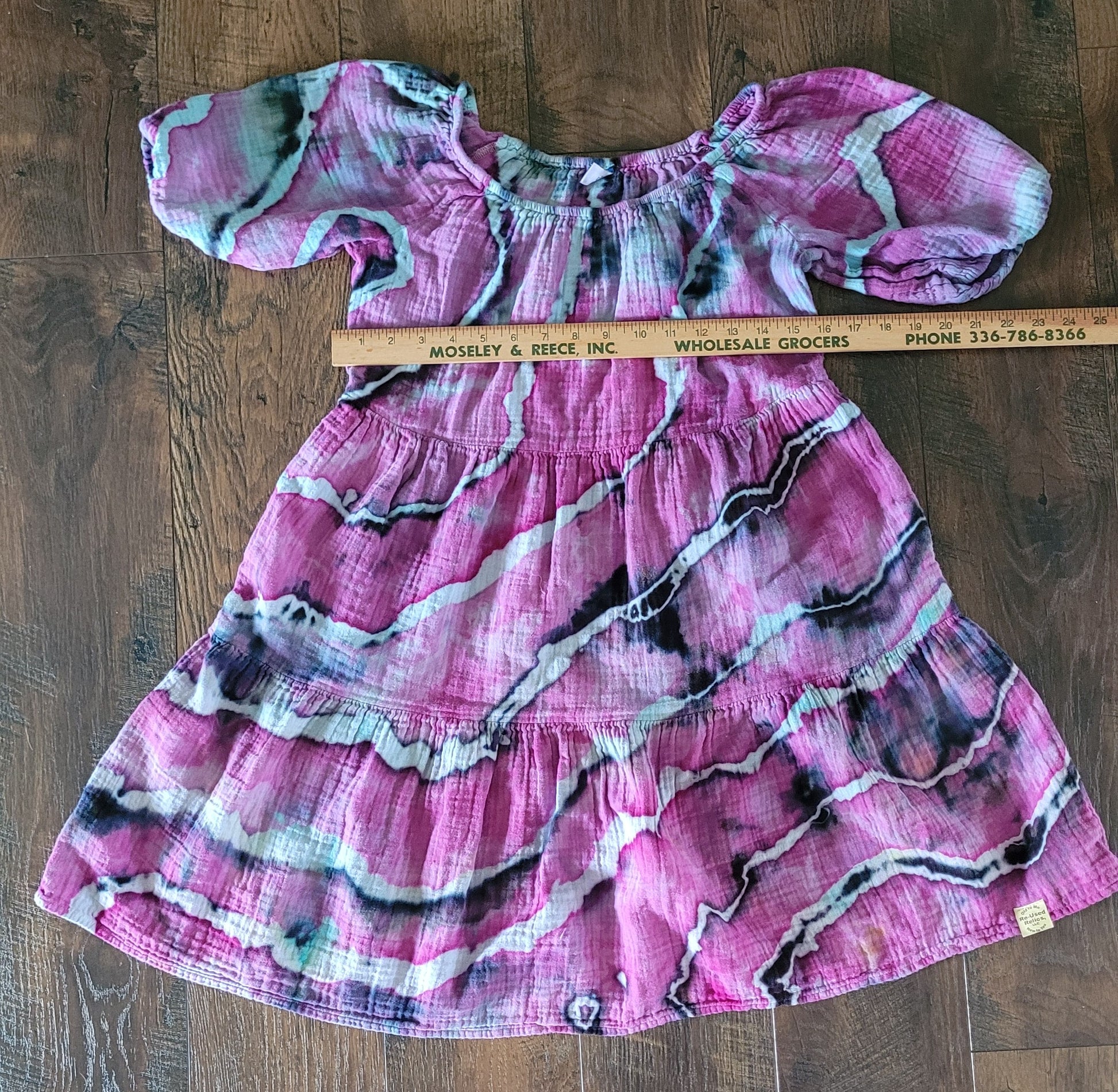 Pink patterned dress on a wooden surface with a ruler for scale.