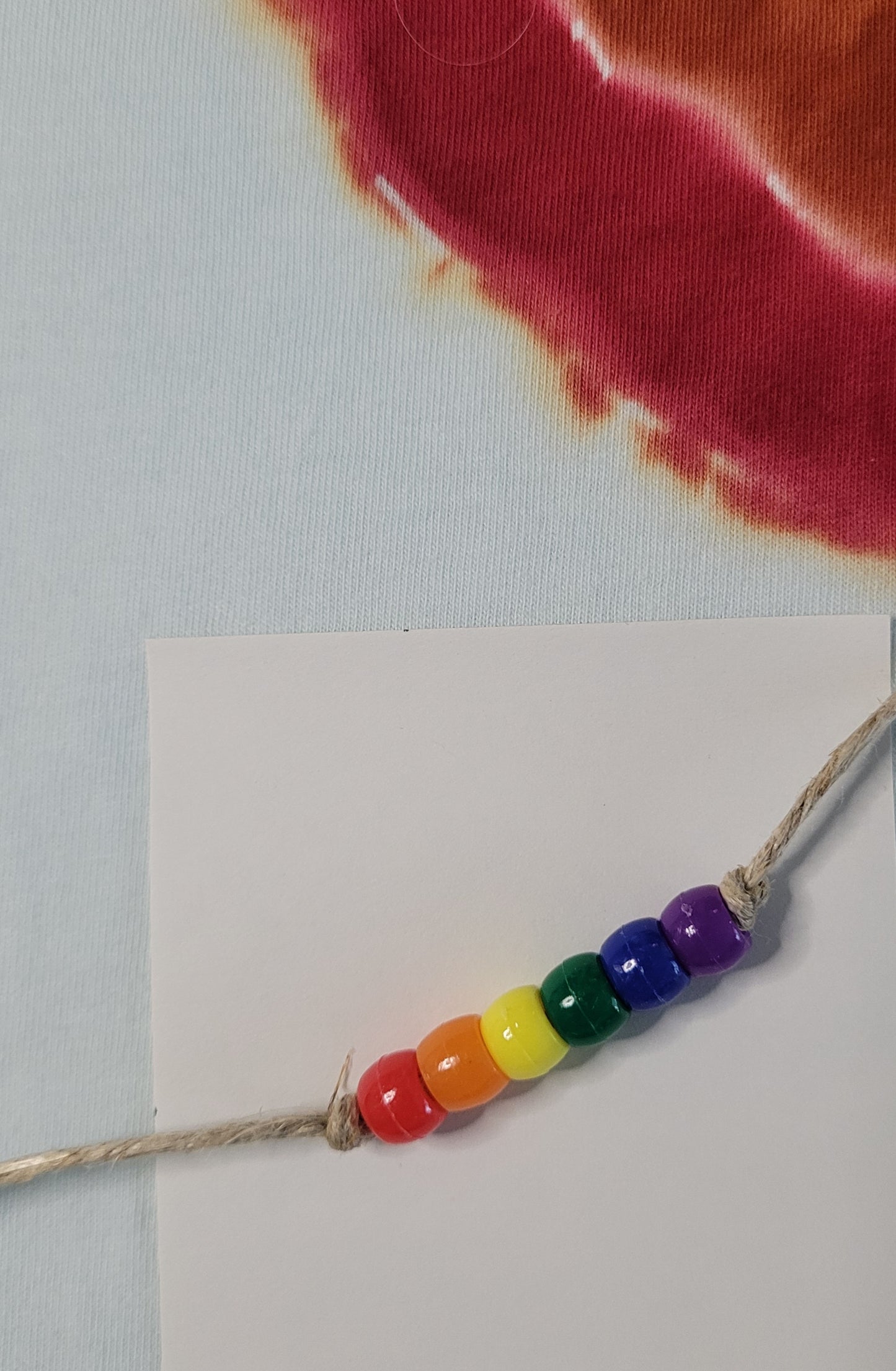 Rainbow beaded bracelet on a white card with tie dye fabric background