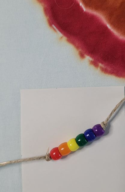Rainbow beaded bracelet on a white card with tie dye fabric background