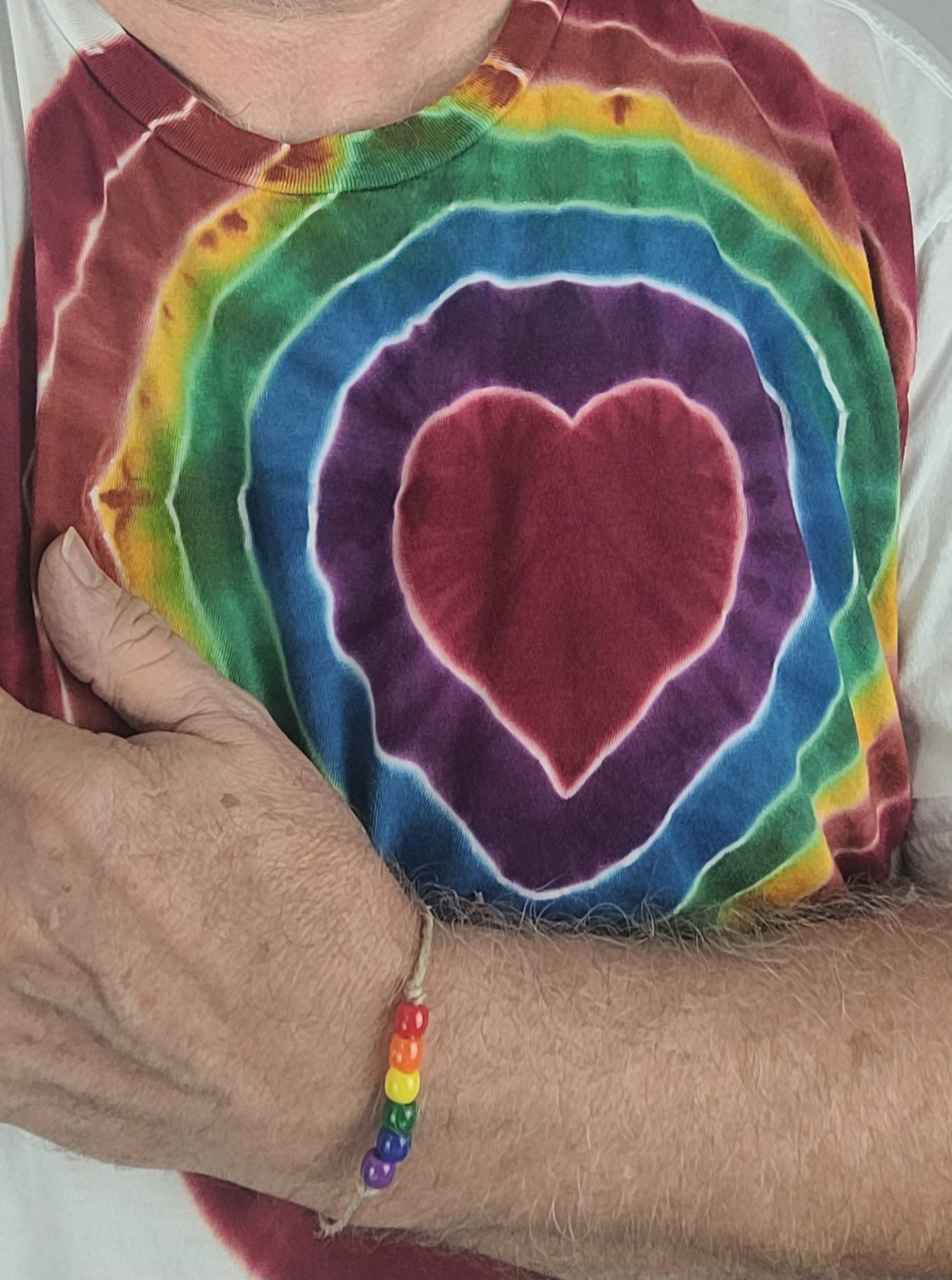 Person wearing a tie-dye shirt with a heart design, holding a rainbow bracelet.