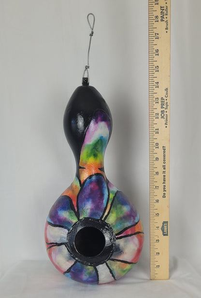 Colorful birdhouse with a black base next to a ruler on a gray background
