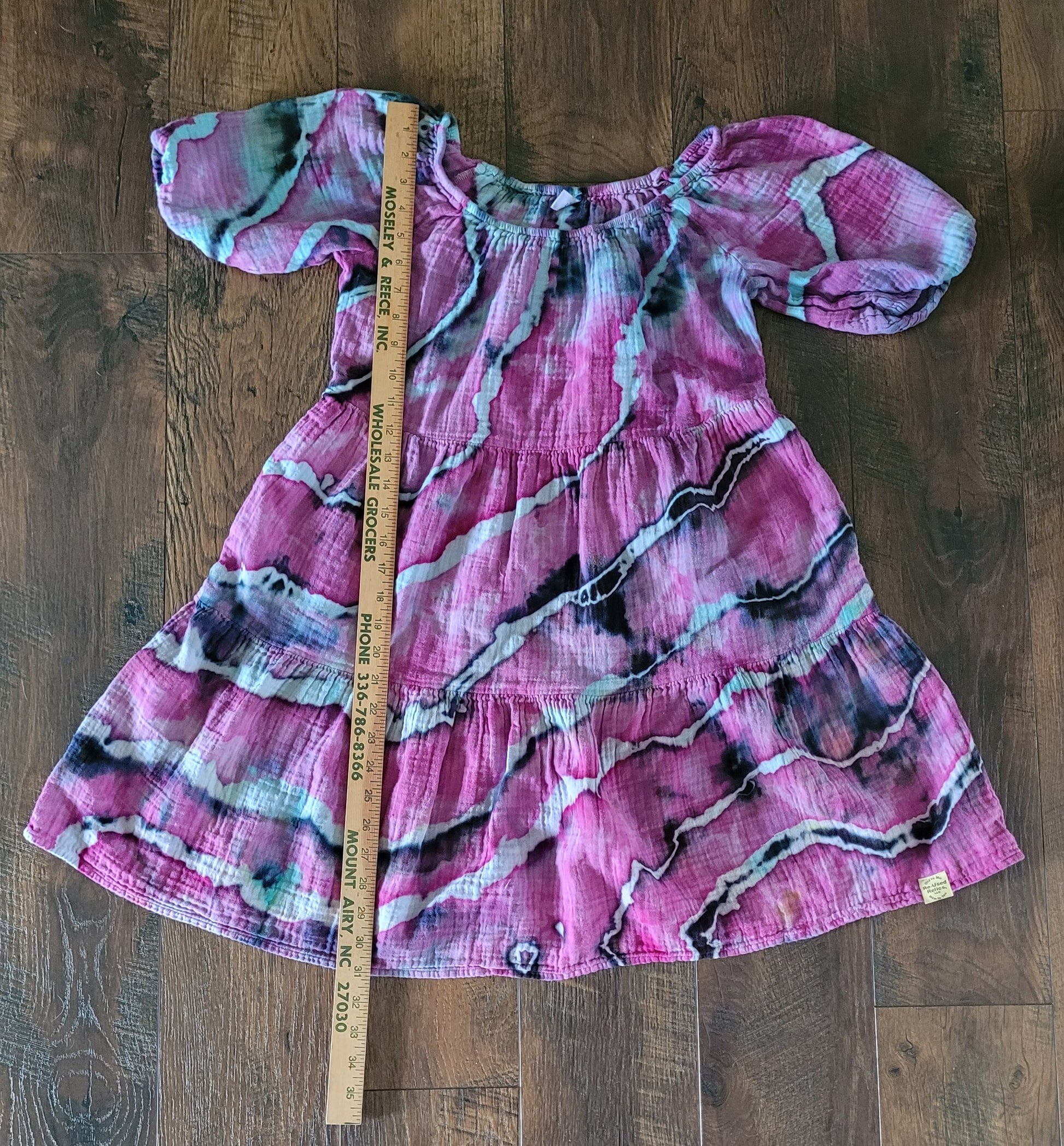 Pink patterned dress on a wooden surface with a ruler for scale.