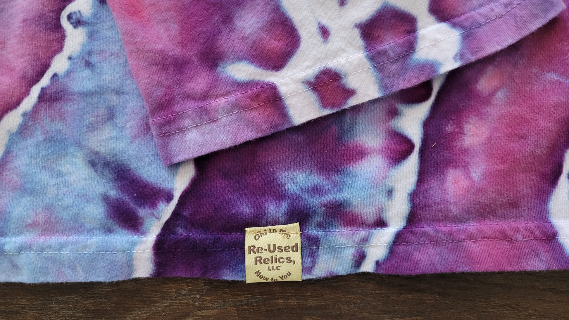 Stack of tie-dye fabric with a 'Re-Used Relics' tag on a wooden surface