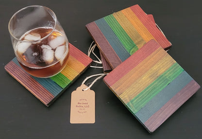 Set of rainbow-colored coasters with a glass of iced tea on a dark surface.