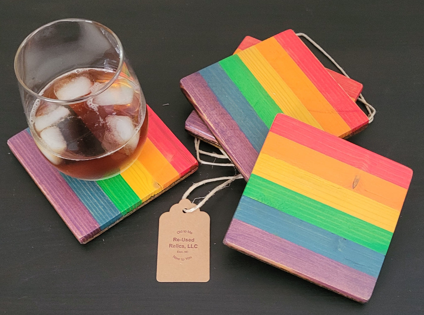 Set of rainbow-colored coasters with a glass of iced tea on a dark surface.