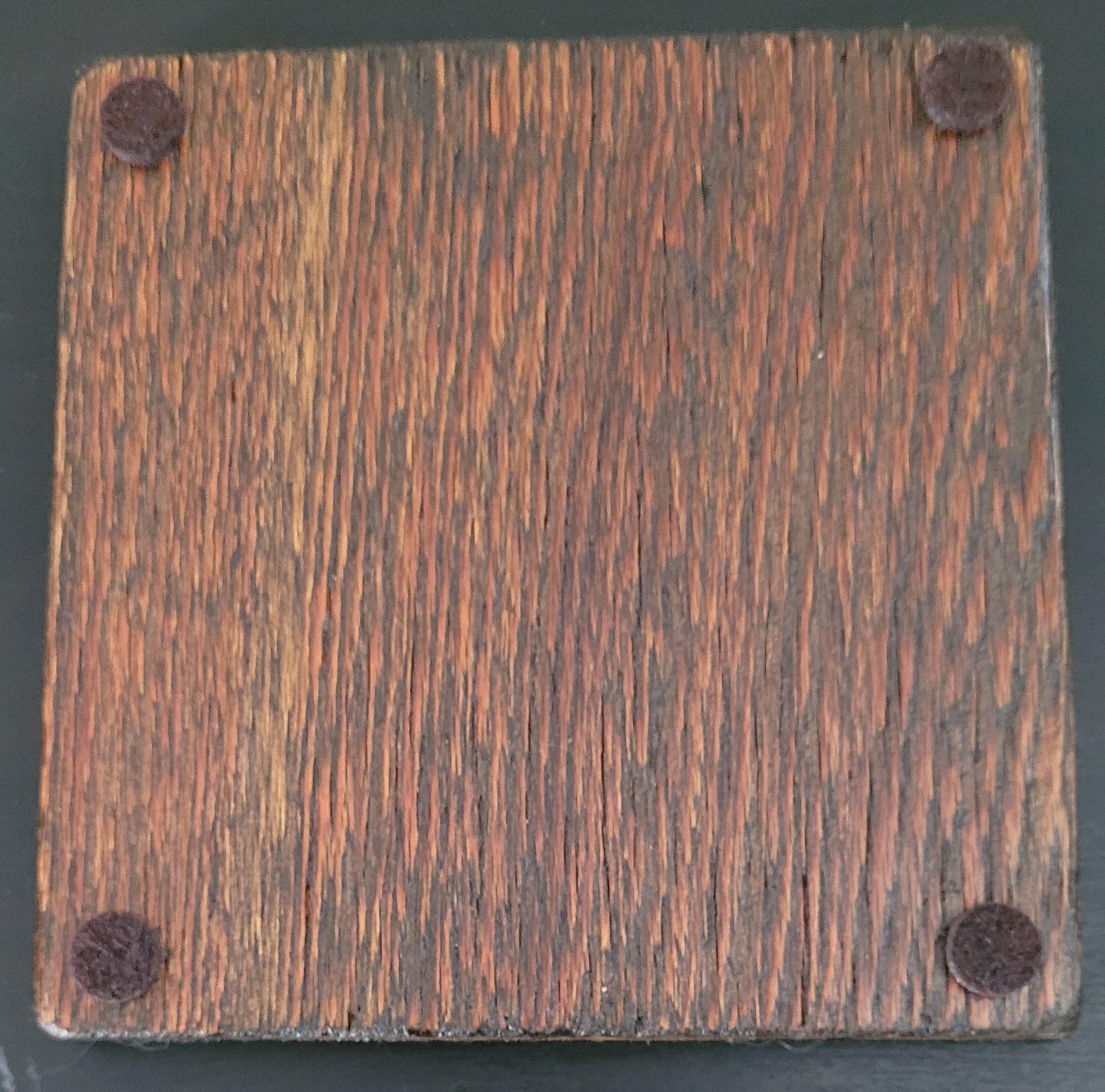 Square wooden coaster bottom with four felt pads  on a dark background