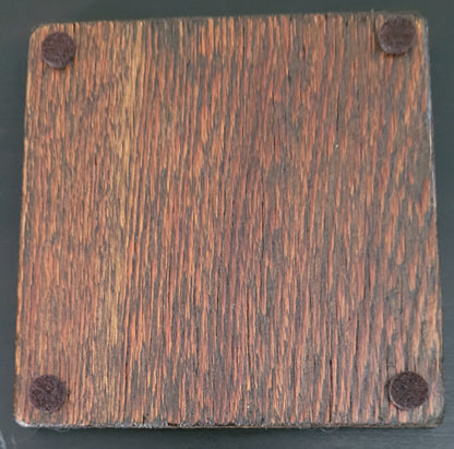 Square wooden coaster bottom with four felt pads  on a dark background