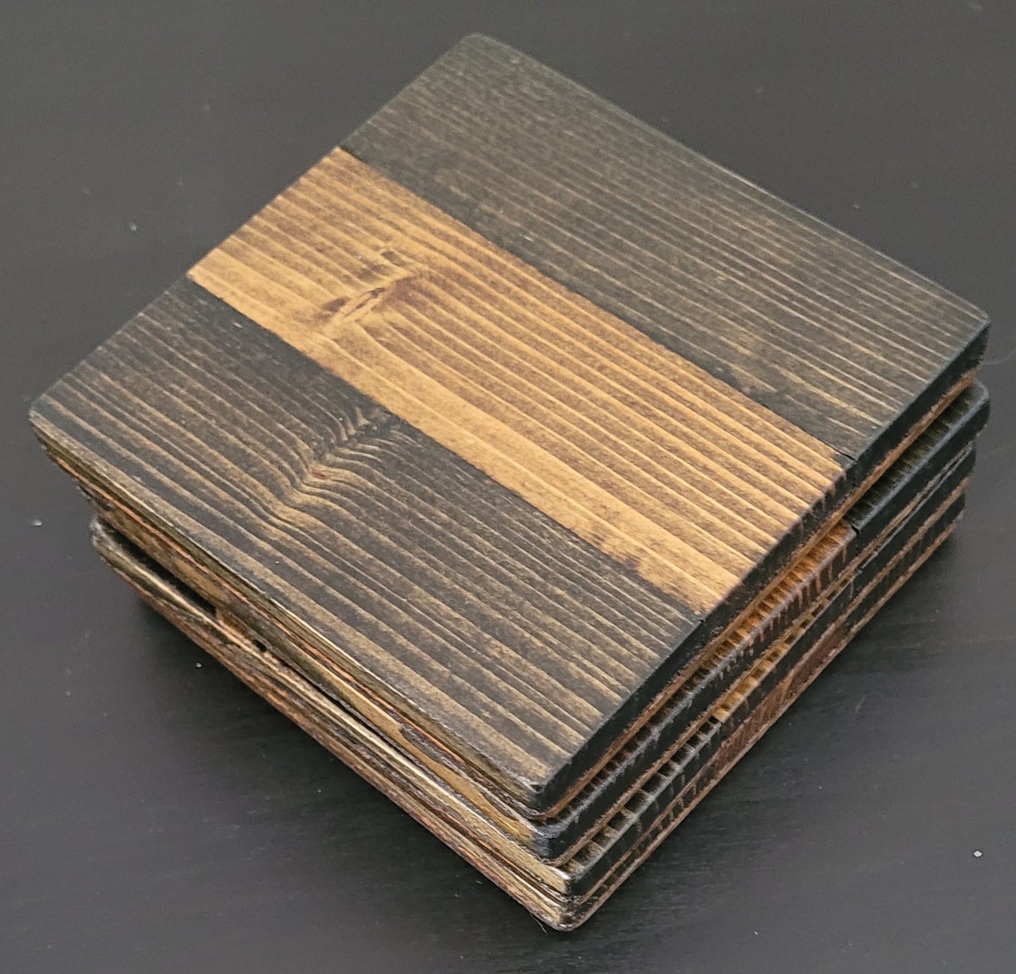Stack of square wooden coasters with a striped pattern on a dark surface