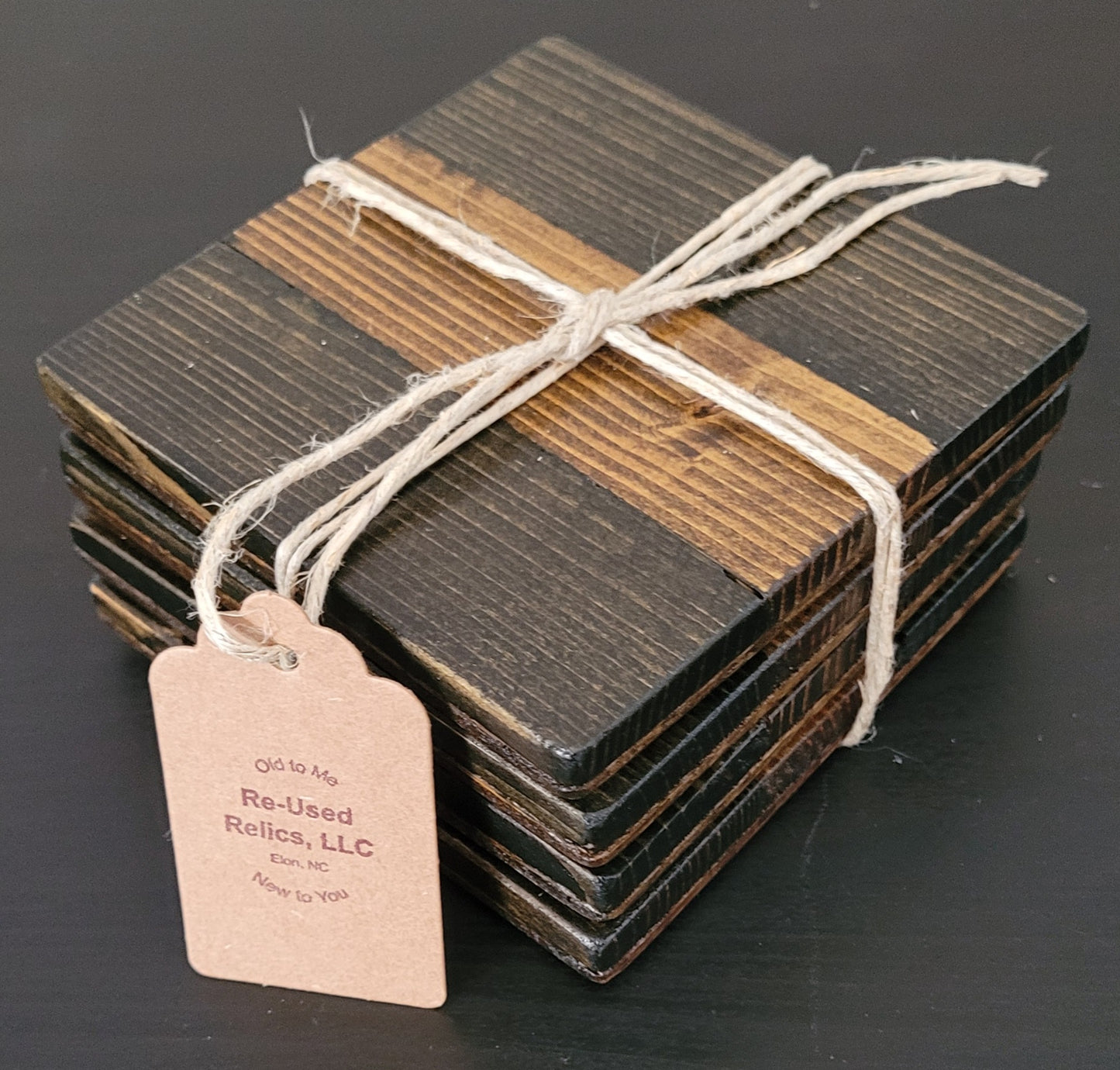 Stack of wooden coasters tied with string on a dark surface, with a tag from Re-Used Relics, LLC.