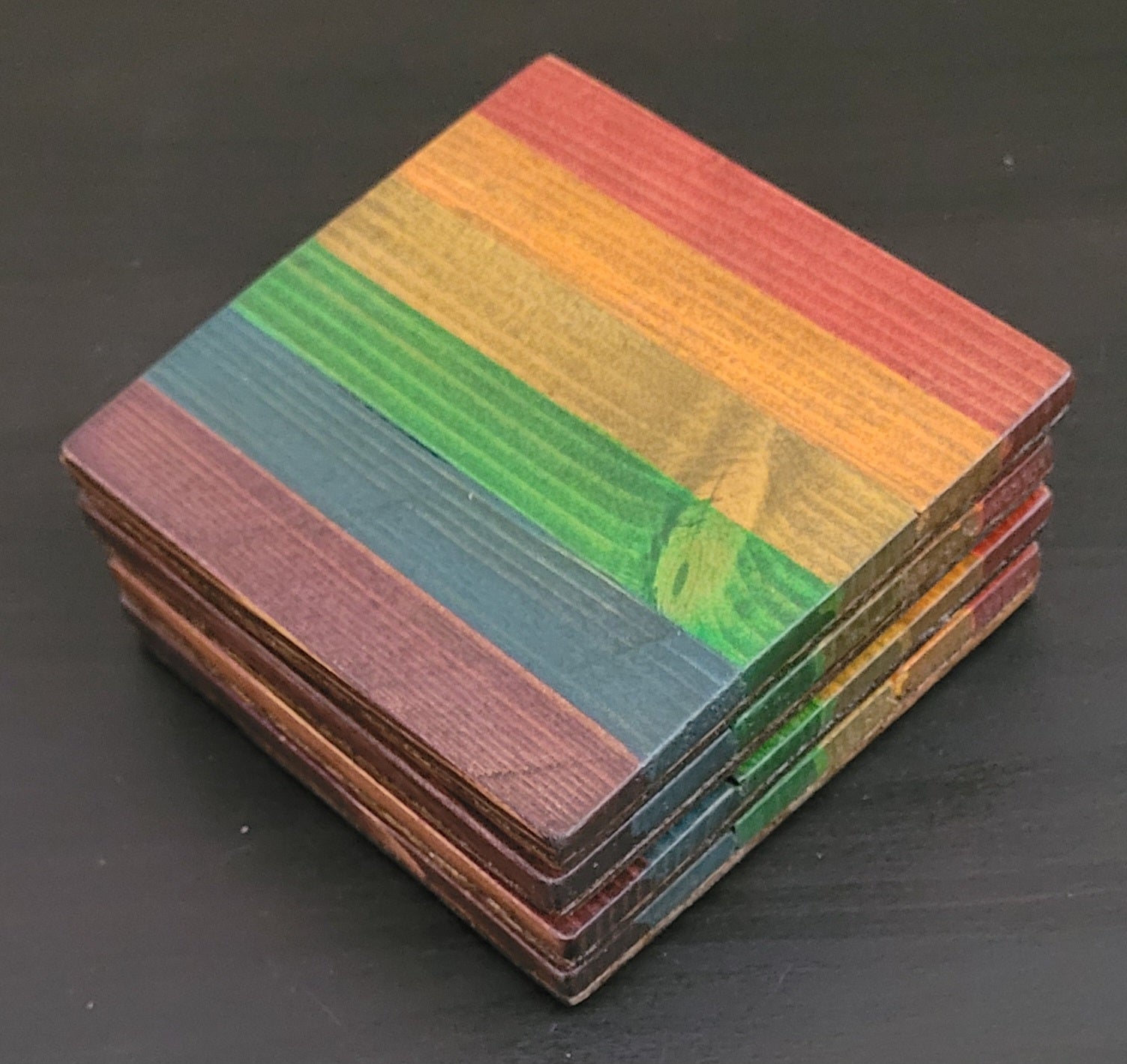 Stack of colorful wooden coasters on a dark surface