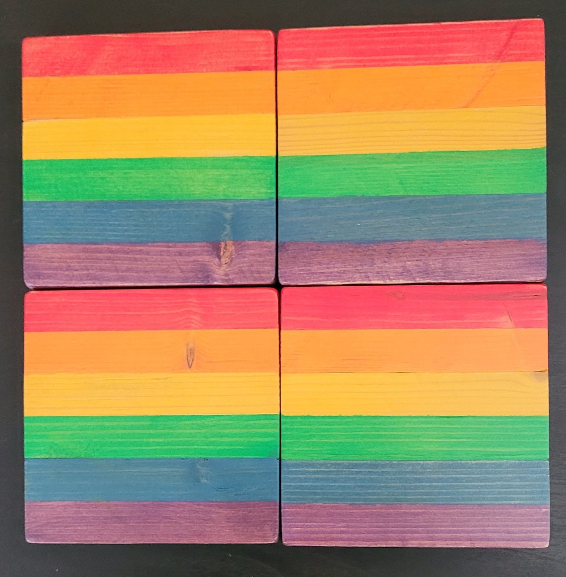 Four wooden coasters with rainbow color pattern on a black background