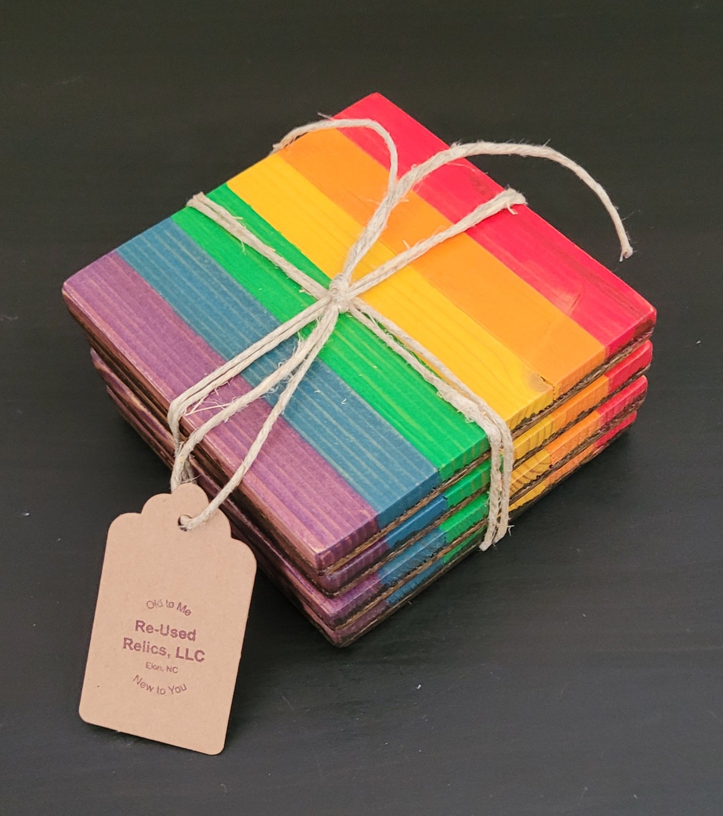Stack of rainbow-colored coasters tied with twine on a black background, with a tag from Re-Used Relics, LLC.
