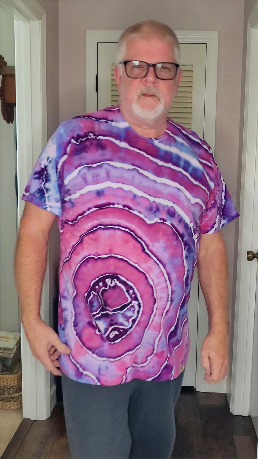 Man wearing a tie-dye shirt with pink and purple patterns in a room.