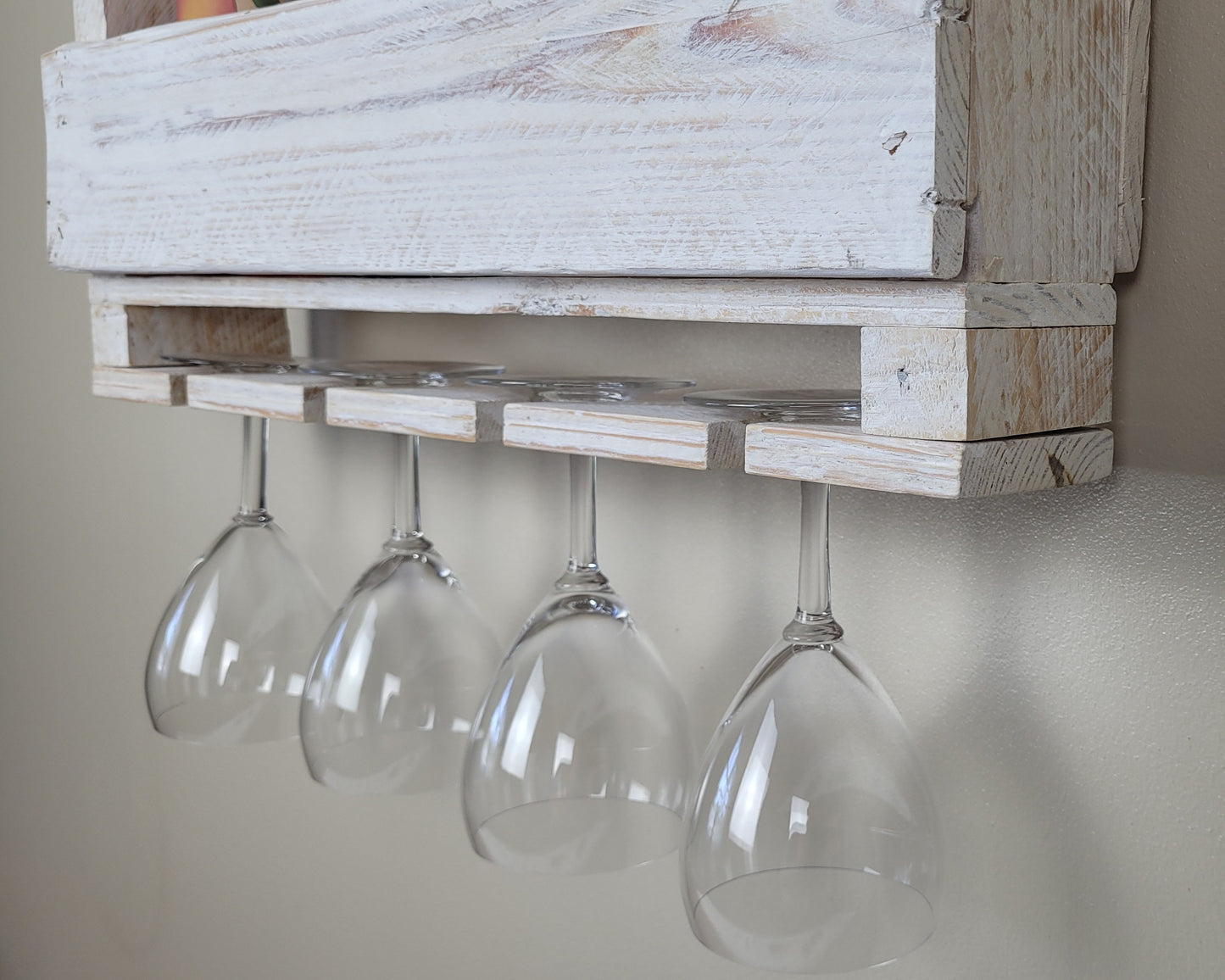 White washed wooden wine rack with four hanging glasses against a neutral wall.