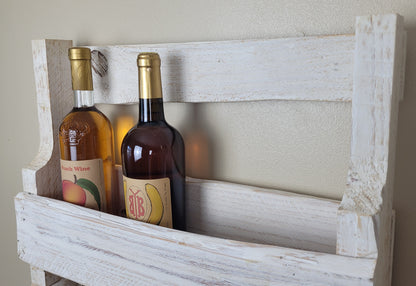 Two wine bottles in a rustic wooden holder against a plain wall.